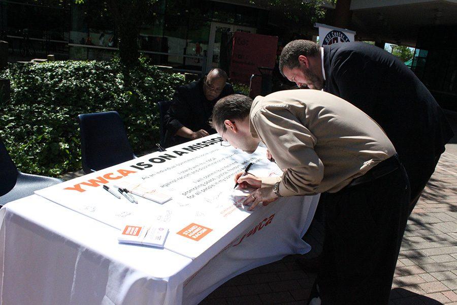 Dean of Students Brian Rush and counselor Thomas Longwell sign the poster which states that they will stand against racism or discrimination of any kind during the Stand Against Racism rally put on by the YWCA on Thursday.