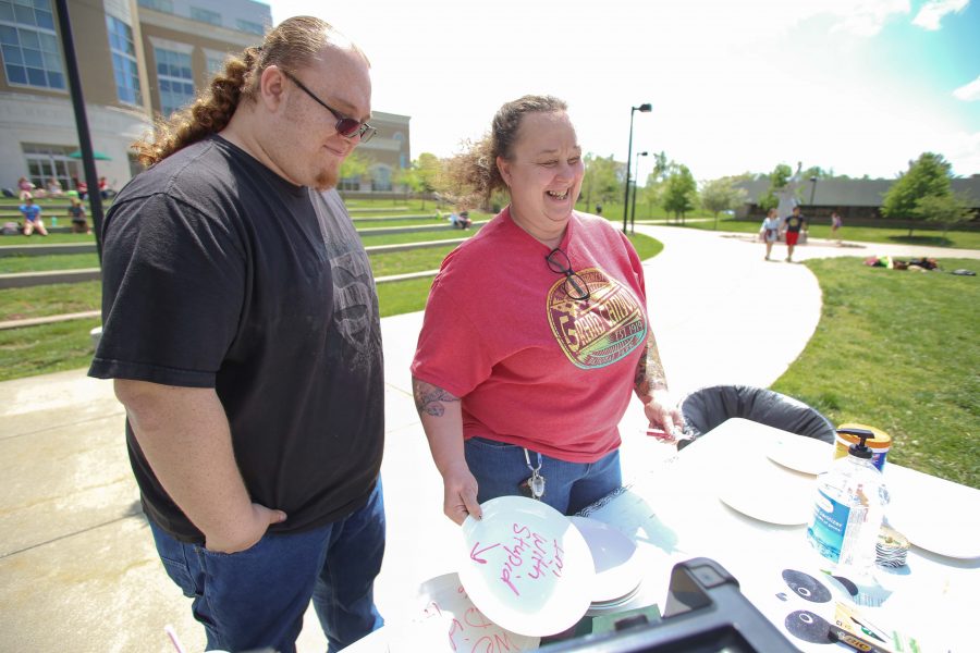 Senior art major Denise “Mickie” Streets laughs as her son Scott Streets, also an art major looks down at her plate that reads “I’m with stupid,” before throwing plates during the Smashing Barriers to Education event Monday at the Quad. Both Mickie and Scott participated in commencement at the Physical Activities Center Saturday. 