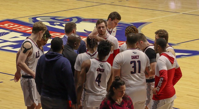The mens basketball team gathers around Coach Stan Gouard during a timeout.