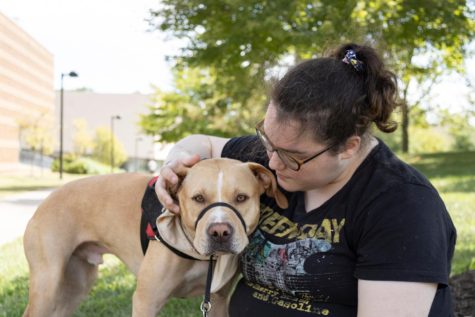 Ness Calloway, senior English teaching major, sits on the grass next to the University Center Fountain while their service dog, Ozzie, performs a task Sept. 1. Ozzie started service dog training when he was 1 year old. (Photo by Crystal Killian)