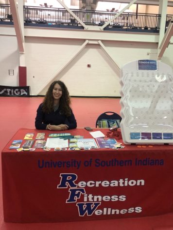 Catherine Champagne, assistant program director for Student Wellness, smiles from behind the Recreation. Fitness and Wellness booth at Condom Carnival Wednesday in the RFWC. (Photo by Alyssa DeWig)