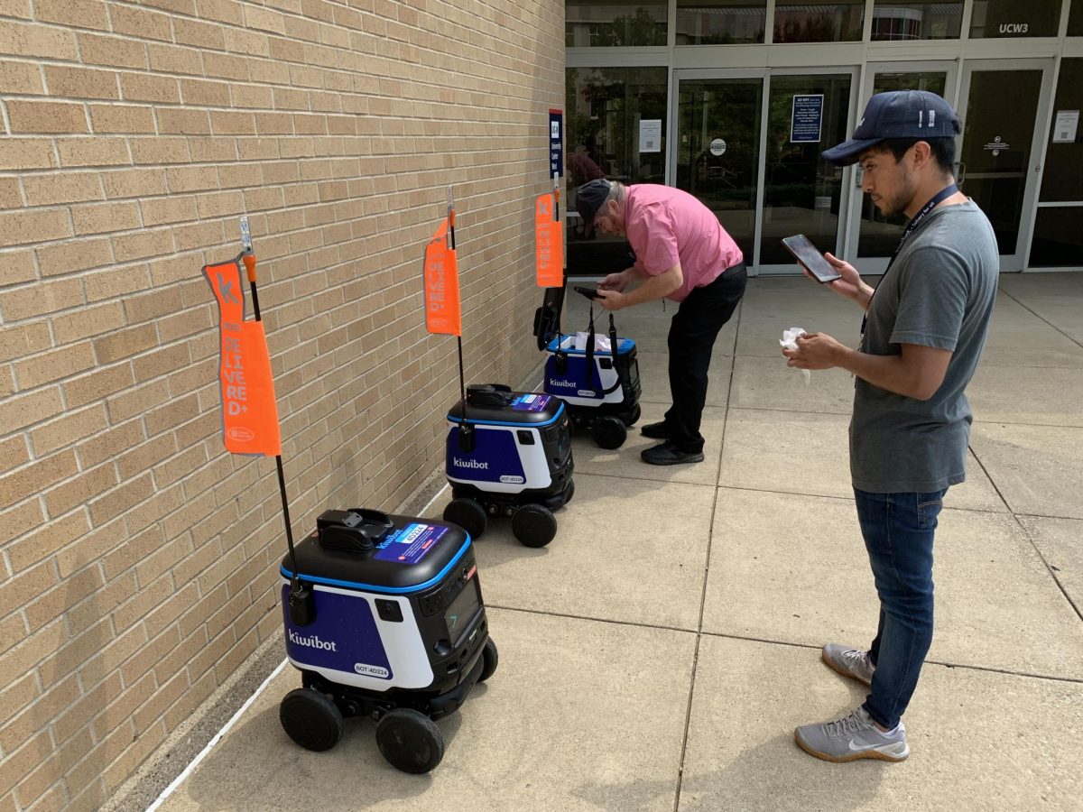 Daniel Goodloe, Chick-fil-A supervisor, and Juan Camilo, Kiwibot intern, place a Chick-fil-A meal inside of a Kiwibot delivery robot in front of University Center West Aug. 22.