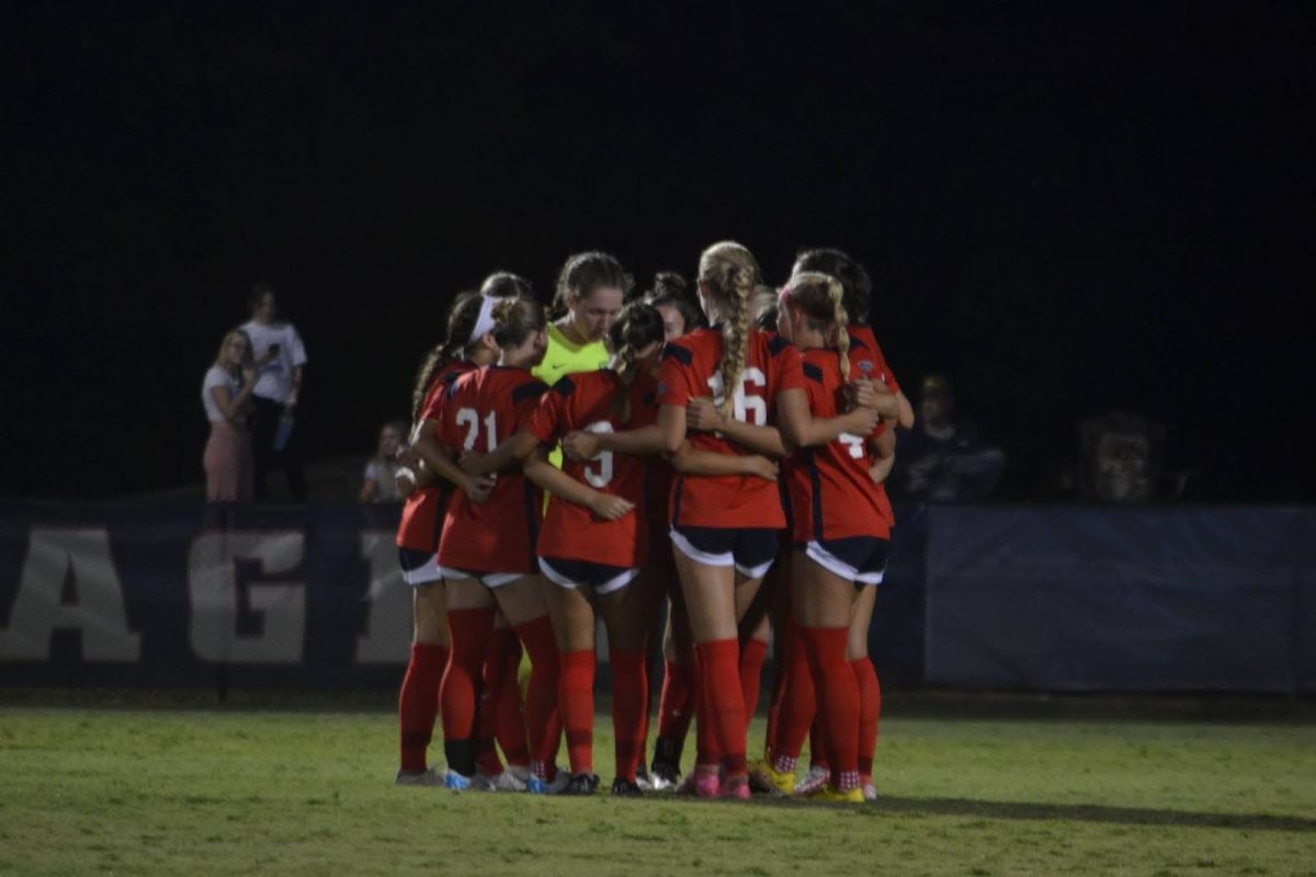 The women’s soccer team huddles with its starting players before the second half against Robert Morris University Thursday at Strassweg Field. (Photo by Alex Mendoza)
