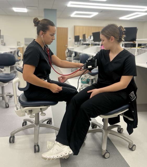 Ashlyn Peach, senior dental assisting major, and Madison Wagner, sophomore dental assisting major, take turns checking each other’s vitals before class Sept. 18. After receiving a $6 million leadership gift from alumnus Wayne Kinney and his family, the College of Nursing and Health Professions building will be renamed  the Kinney College of Nursing and Health Professions.