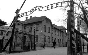 The entrance to Auschwitz with an inscription that reads “Work Sets You Free” above it. 
