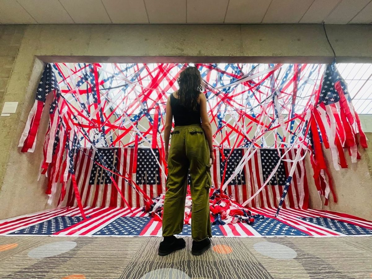 Bailey Roby, fine arts graduate, stands in front of her art piece, “America: Land of the…,” April 27 in the Arts Center.