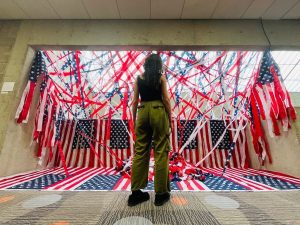 Bailey Roby, fine arts graduate, stands in front of her art piece, “America: Land of the…,” April 27 in the Arts Center.
