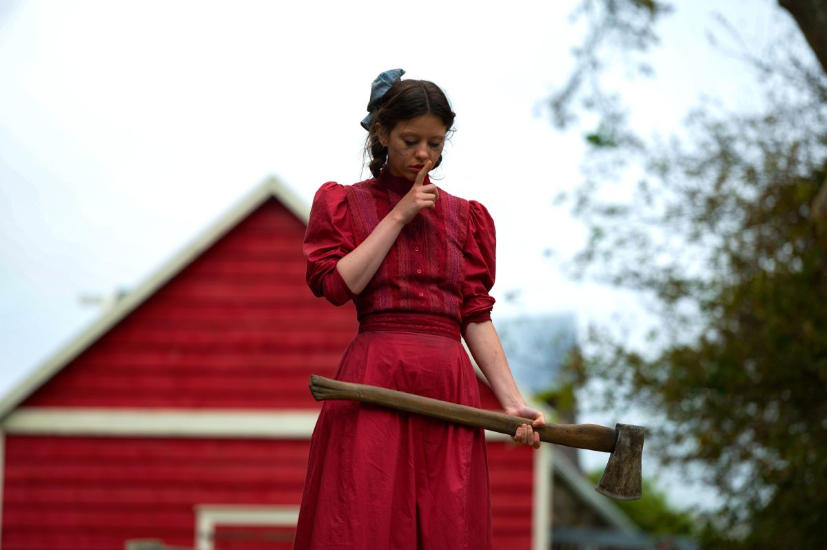 Pearl stands outside, wearing a red dress and holding an axe in “Pearl” (2022). 