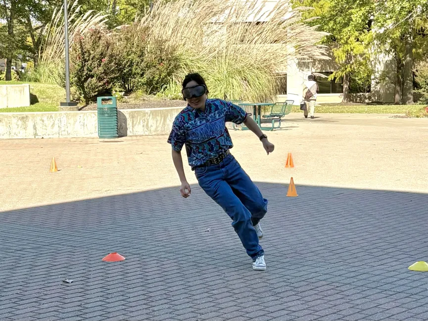 Delaney Anthis, junior exercise science pre-physical therapy major, runs through the tricycle course while wearing vision impairment goggles in the breezeway Wednesday, Oct. 21.