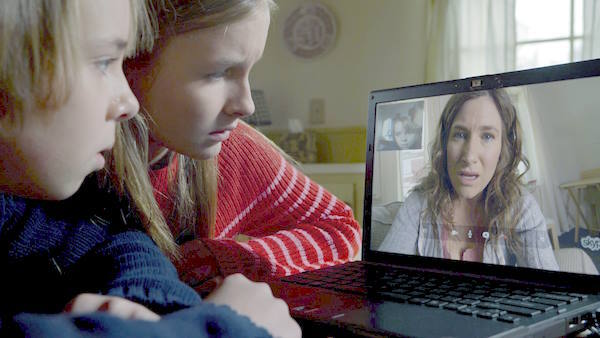 Becca (Olivia DeJonge) and Tyler (Ed Oxenbould) gather around a video call with their mother (Kathryn Hahn), where she reveals the disturbing truth about the children’s grandparents. 