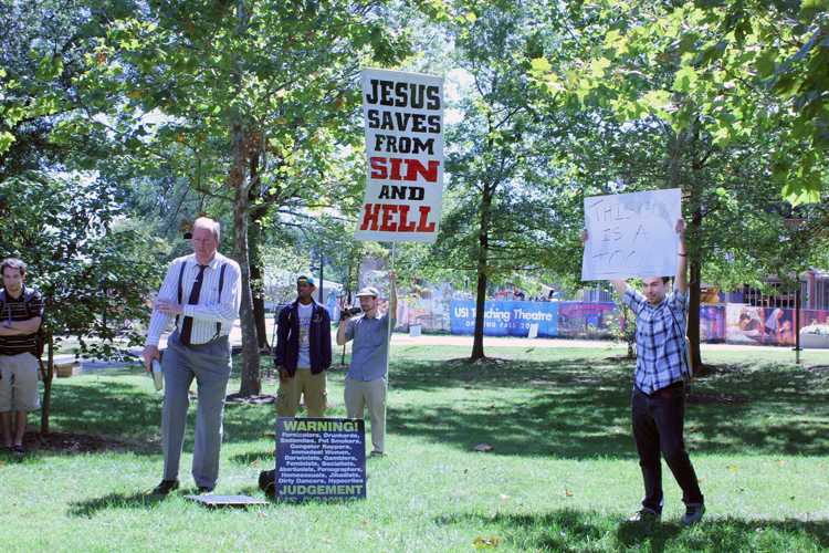 Street evangelist James Gilles (left) preaches to a crowd on campus Monday, which prompted USI student Spencer Kiessling (right) to create the sign he’s holding.